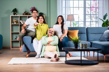 Dört kişilik Hintli bir aile kanepede televizyon seyrediyor, uzaktan kumandayla kanal değiştiriyor.