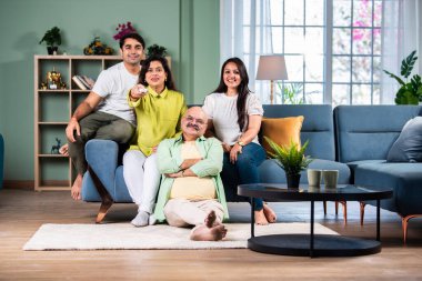 Dört kişilik Hintli bir aile kanepede televizyon seyrediyor, uzaktan kumandayla kanal değiştiriyor.