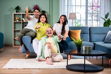 Dört kişilik Hintli bir aile kanepede televizyon seyrediyor, uzaktan kumandayla kanal değiştiriyor.