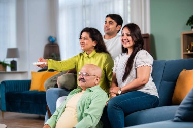 Dört kişilik Hintli bir aile kanepede televizyon seyrediyor, uzaktan kumandayla kanal değiştiriyor.