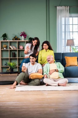 Neşeli Hintli aile evde akıllı telefon kullanırken eğleniyor.