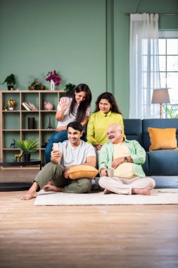 Neşeli Hintli aile evde akıllı telefon kullanırken eğleniyor.