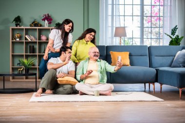 Neşeli Hintli aile evde akıllı telefon kullanırken eğleniyor.