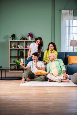 Neşeli Hintli aile evde akıllı telefon kullanırken eğleniyor.