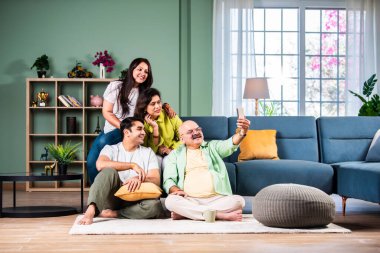 Neşeli Hintli aile evde akıllı telefon kullanırken eğleniyor.