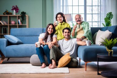 Neşeli Hintli aile evde çay ya da kahve içerken kameraya bakıyorlar.