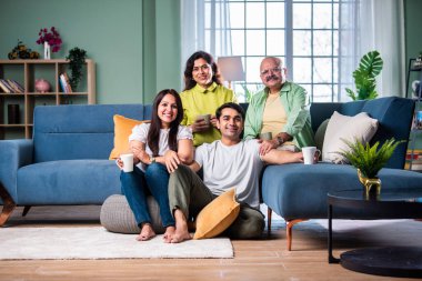 Neşeli Hintli aile evde çay ya da kahve içerken kameraya bakıyorlar.