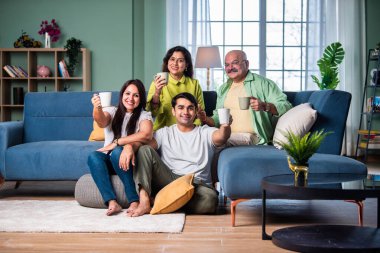 Neşeli Hintli aile evde çay ya da kahve içerken kameraya bakıyorlar.