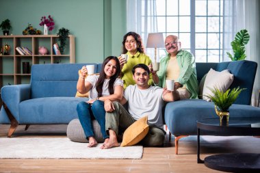 Neşeli Hintli aile evde çay ya da kahve içerken kameraya bakıyorlar.