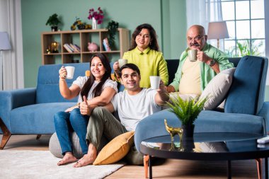 Neşeli Hintli aile evde çay ya da kahve içerken kameraya bakıyorlar.