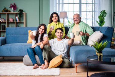 Neşeli Hintli aile evde çay ya da kahve içerken kameraya bakıyorlar.