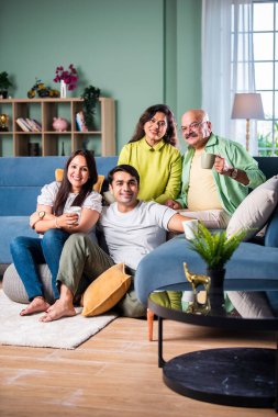 Neşeli Hintli aile evde çay ya da kahve içerken kameraya bakıyorlar.