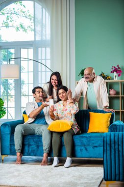 Neşeli Hintli aile evde akıllı telefon kullanırken eğleniyor.