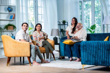 Modern evdeki oturma odasında grup fotoğrafı için poz veren dört kişilik Hintli aile.