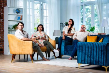 Modern evdeki oturma odasında grup fotoğrafı için poz veren dört kişilik Hintli aile.