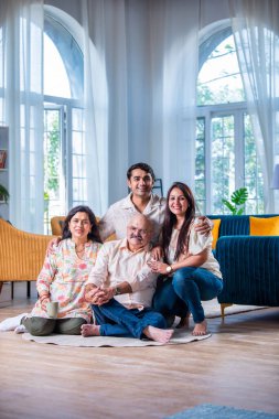 Modern evdeki oturma odasında grup fotoğrafı için poz veren dört kişilik Hintli aile.