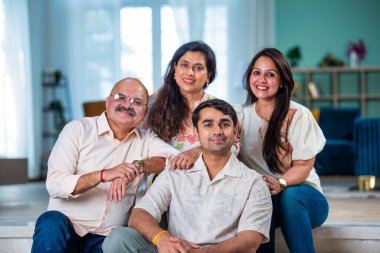 Modern evdeki oturma odasında grup fotoğrafı için poz veren dört kişilik Hintli aile.