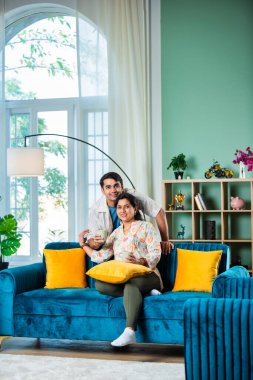 Yakışıklı genç Hintli adam ve yaşlı anne evde kahve içiyorlar.