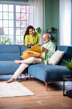 Oturma odasında kanepede oturmuş fotoğraf albümü izleyen kıdemli Hintli çift.