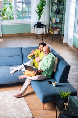 Mutlu Hintli yaşlı çift evde dizüstü bilgisayar kullanıyor ve gülümsüyor.