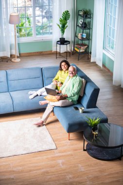 Mutlu Hintli yaşlı çift evde dizüstü bilgisayar kullanıyor ve gülümsüyor.