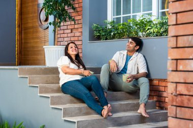 Mutlu Hintli genç çift dışarıda otururken çay ya da kahve içiyorlar.