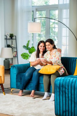 Yetişkin Hintli anne ve yetişkin kızı akıllı telefon kullanıyor.