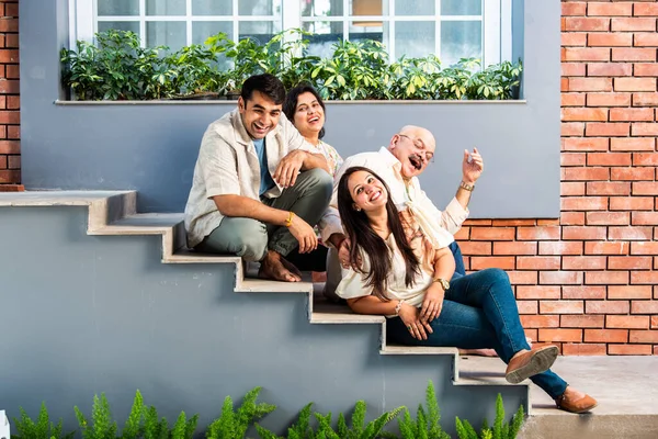 Portrait of happy Indian family of four sitting outdoor on stairs looking at camera