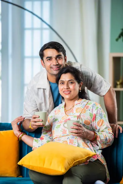 Handsome young adult Indian man and old mother having coffee at home