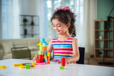 Hintli küçük kız evdeki masada tahta bloklarla oynuyor.