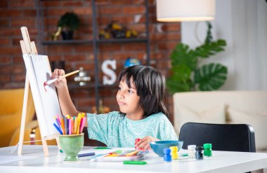 Hintli küçük çocuk fırça ve boya kullanarak Easel ya da kağıt üzerinde resim yapıyor.