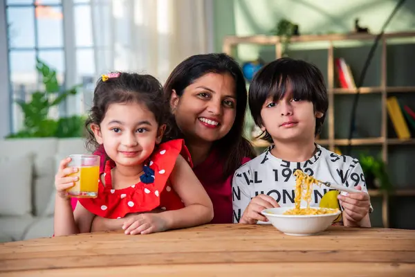 Indian mother and kids having noodles and juice at breakfast table