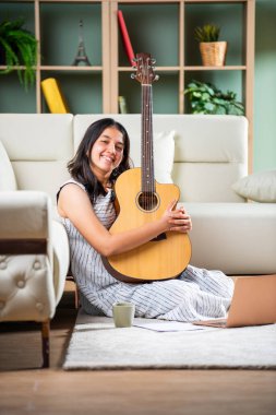 Evde kağıt dizüstü bilgisayarı ve gitarı olan Hintli şarkı yazarı kız.