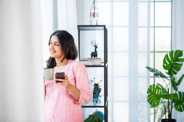 Hintli güzel kız alışveriş için akıllı telefon kullanıyor, oturma odasında tasarruf yapıyor.