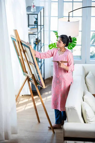 stock image Cheerful Indian young artist girl painting picture at easel in living room