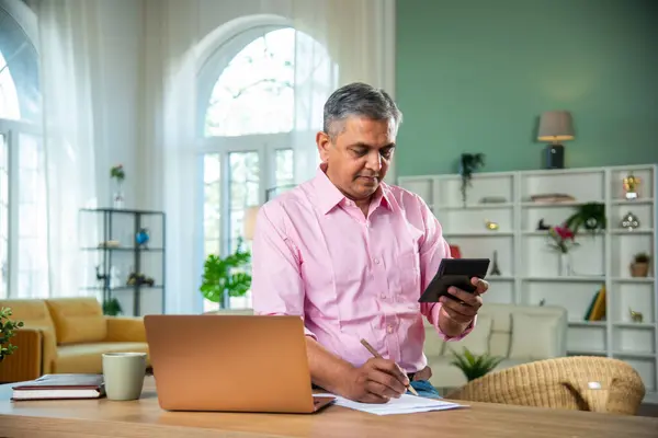 Indian Mid age man working on laptop, smartphone with documents having coffee