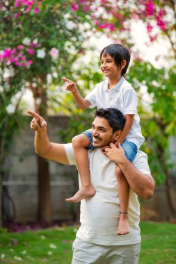 Hintli Asyalı bir babanın portresi. Parkta genç bir çocuğu sırtında taşıyor.