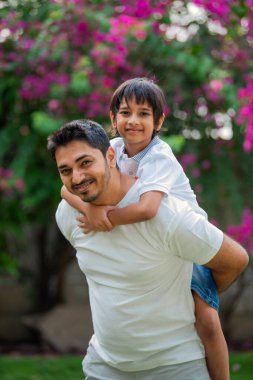 Hintli Asyalı bir babanın portresi. Parkta genç bir çocuğu sırtında taşıyor.
