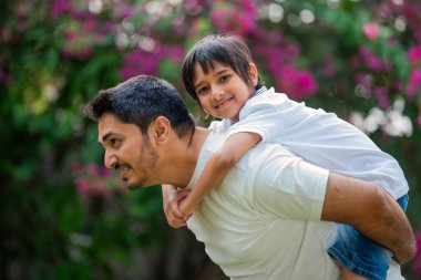 Hintli Asyalı bir babanın portresi. Parkta genç bir çocuğu sırtında taşıyor.