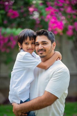 Hintli Asyalı bir babanın portresi. Parkta genç bir çocuğu sırtında taşıyor.
