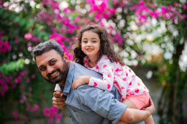 Hintli genç baba parkta küçük kızını taşıyor.