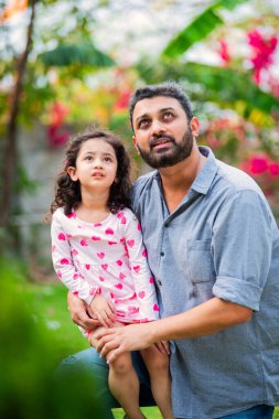 Hintli genç baba parkta küçük kızını taşıyor.