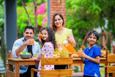 Bahçedeki yemek masasında yemek yiyen dört kişilik Hintli genç bir aile.