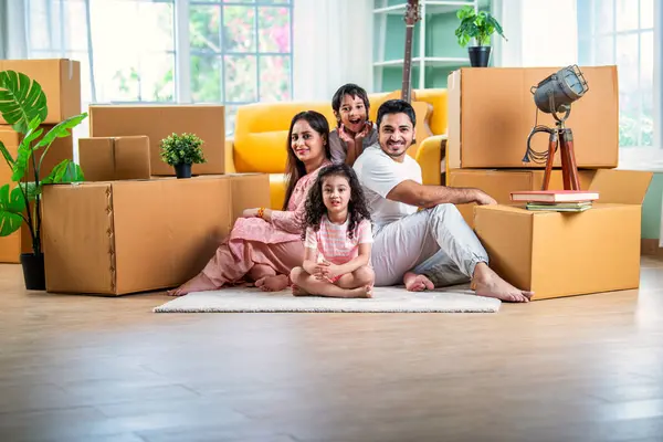 House move concept. Happy Indian young family sitting on the floor in new home