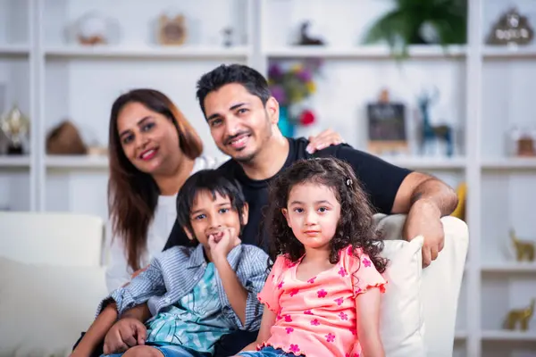 Portrait of Happy indian young family of four sitting on sofa in living room