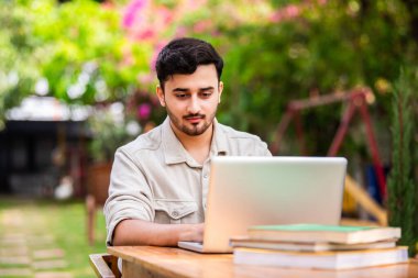 Asyalı Hintli erkek öğrenci ya da serbest çalışan dışarıda masada otururken dizüstü bilgisayar kullanıyor.