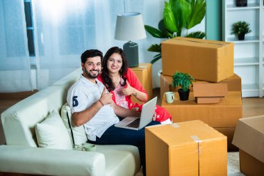 Hintli genç çift kanepeye dizüstü bilgisayar kullanarak taşınıyor ya da konsept değiştiriyor.