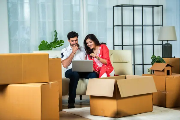 Indian young couple home moving or shifting concept, using laptop on sofa