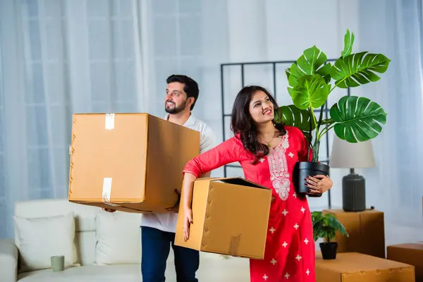 Indian young couple shifting home holding boxes in new home