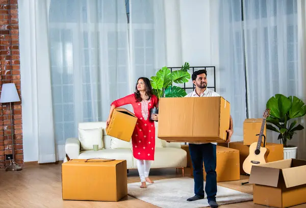 Indian young couple shifting home holding boxes in new home